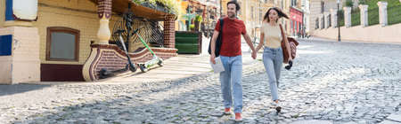 Couple of travelers with map and binoculars holding hands while walking on urban street, bannerの写真素材