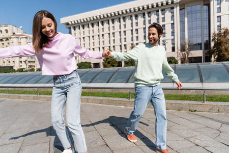 Smiling man holding hand of girlfriend riding penny board on urban streetの写真素材