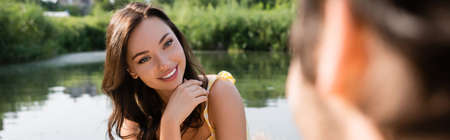 cheerful woman flirting and looking at blurred boyfriend, banner
