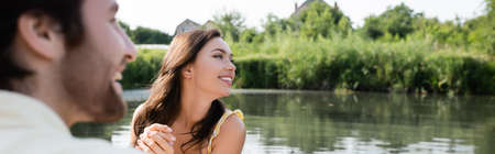 happy woman smiling and looking away near cheerful and blurred boyfriend, banner