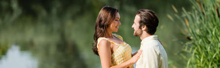 happy young couple looking at each other near lake, banner