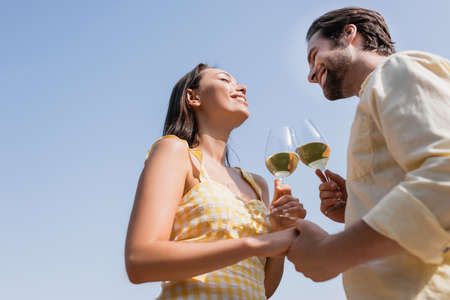 low angle view of young couple in summer clothes clinking glasses with wineの写真素材