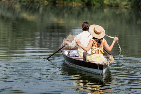 back view of woman in straw hat having boat ride with boyfriend