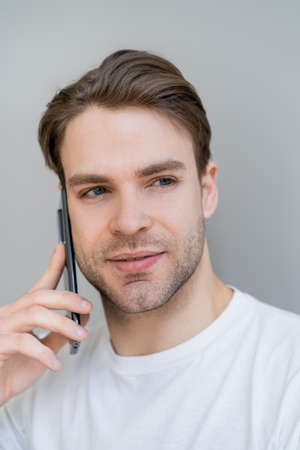 portrait of young man looking away during conversation on smartphone isolated on grey
