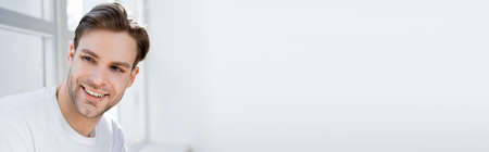 portrait of young and joyful man looking away near white wall, bannerの写真素材