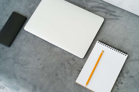 top view of closed laptop, empty notebook with pencil and smartphone with blank screen on grey...
