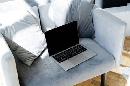laptop with blank screen near soft pillows on grey armchair