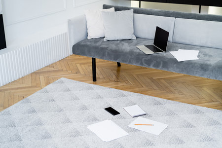 laptop, smartphone and empty papers on sofa and floor in living room