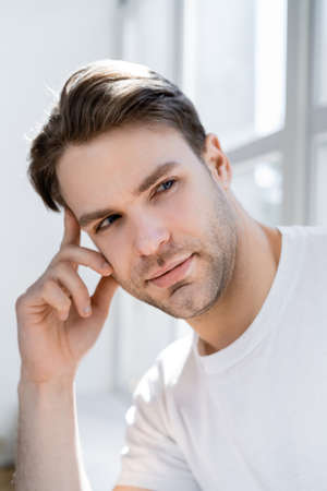 dreamy and positive man holding hand near face while looking awayの写真素材