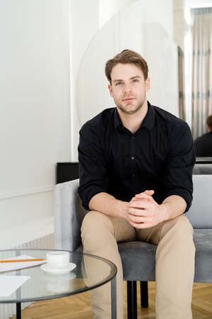 man in black shirt looking at camera while sitting on sofa near coffee table