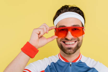 Happy sportsman holding sunglasses and looking at camera isolated on yellowの写真素材