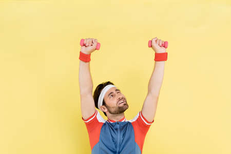 Brunette sportsman lifting dumbbells and looking up isolated on yellow