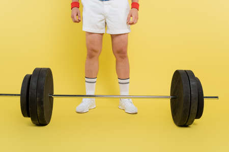 Cropped view of barbell near sportsman standing on yellow background