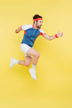 Bearded sportsman jumping and looking away isolated on yellowの写真素材