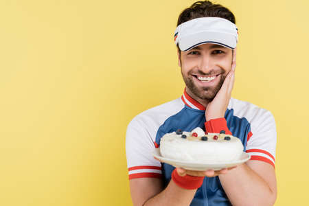 Positive sportsman in visor holding blurred cake isolated on yellowの写真素材