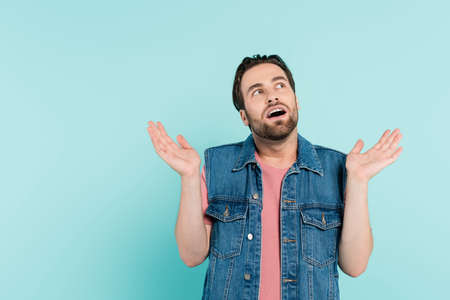 Shocked man in denim vest looking away isolated on blue