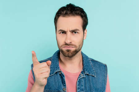 Serious man looking and pointing with finger at camera isolated on blue