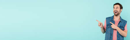 Positive man pointing with fingers isolated on blue with copy space, banner