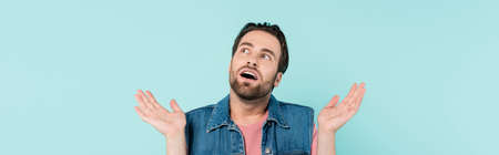 Young shocked man looking away isolated on blue, banner