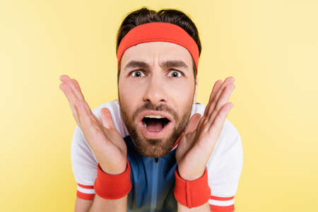 Portrait of shocked sportsman looking at camera isolated on yellow