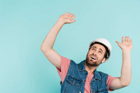 Scared man in hardhat looking up isolated on blue