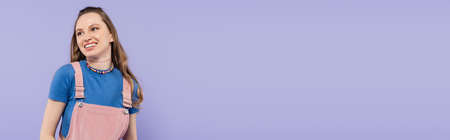 cheerful woman in overall dress isolated on purple, banner