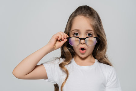 astonished girl looking at camera over eyeglasses isolated on greyの写真素材