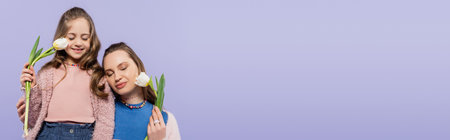 pleased mother and daughter with closed eyes holding tulips isolated on purple, bannerの写真素材