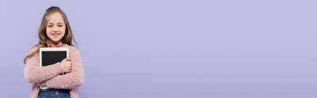 joyful girl hugging digital tablet with blank screen isolated on purple, banner