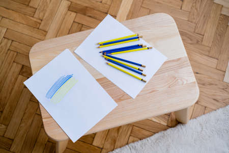 top view of blue and yellow pencils near white paper with ukrainian flag on wooden tableの写真素材