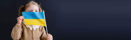 patriotic child obscuring face with small ukrainian flag isolated on black with copy space, bannerの写真素材