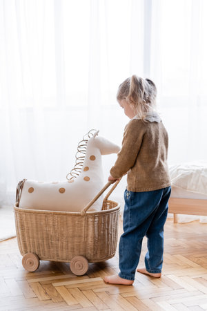 full length view of barefoot girl playing with toy horse in wicker cart at homeの写真素材