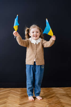 full length view of joyful patriotic child holding ukrainian flags near black wallの写真素材