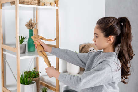 side view of girl playing with toy human figurine near rack with potted plantsの写真素材