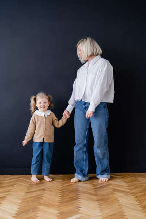 full length view of barefoot mother and daughter holding hands near black wall at homeの写真素材