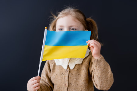 little girl obscuring face with small ukrainian flag isolated on blackの写真素材
