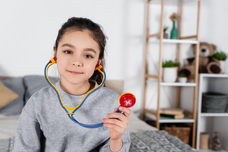 cheerful brunette girl with toy stethoscope smiling at cameraの写真素材