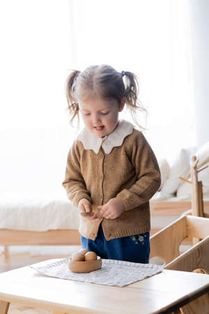 girl sticking out tongue while holdings spoon near bowl with wooden ballsの写真素材