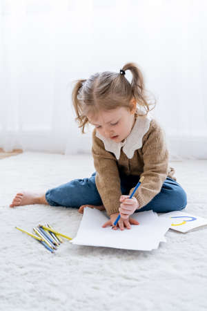 little girl with ponytails drawing on floor near card with blue and yellow heart