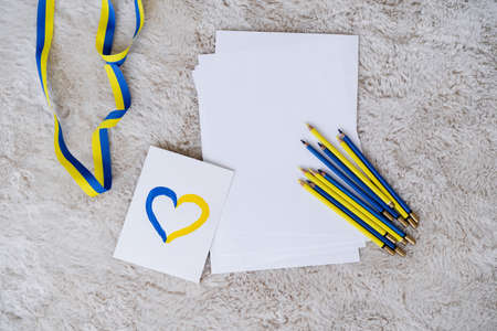 top view of color pencils, ribbon and card with blue and yellow heart on grey fluffy carpet