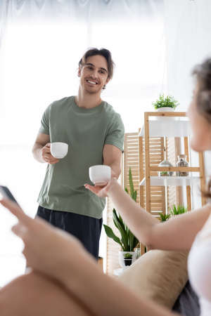happy man holding cups of coffee near blurred girlfriend