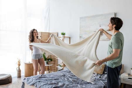 happy young couple covering bed with blanketの写真素材