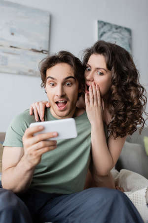 shocked man and woman looking at smartphone at homeの写真素材