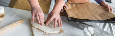Cropped view of teenager making cookie near friend with baking sheet at home, bannerの写真素材