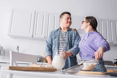 Low angle view of teenager with down syndrome cooking near boyfriend at homeの写真素材
