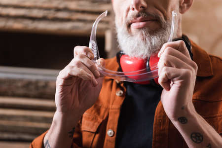 cropped view of bearded woodworker holding googles in workshop