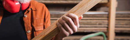 partial view of furniture designer holding plank in carpentry workshop, banner