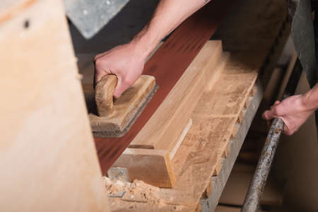 partial view of woodworker polishing board on sander machine