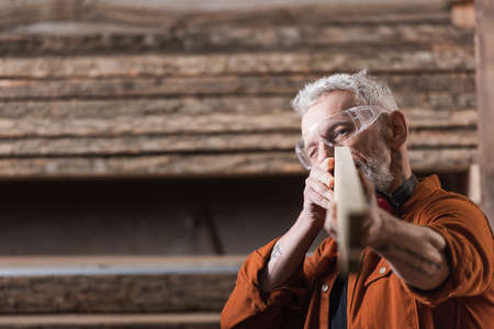 middle aged carpenter checking blurred plank in workshop