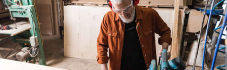 bearded carpenter in eyeglasses working with miter saw in workshop, bannerの写真素材